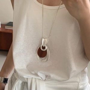 Necklace with silver hollow droplet and brown textured wood disc on white shirt