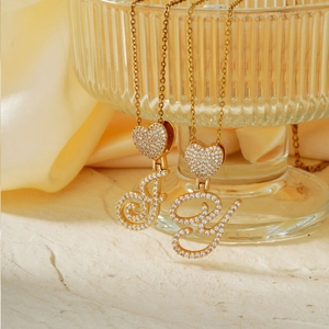 Gold plated heart necklace with zircon inlay and cursive letters on a glass edge
