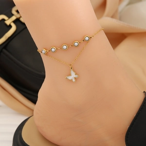 Double-layer gold anklet with white beads and butterfly pendant worn on ankle
