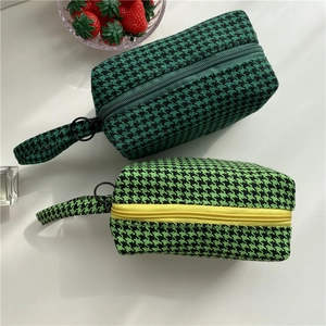 Macro detail of houndstooth fabric pouches with circular zipper pulls and carrying straps