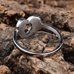 Brushed stainless steel wing ring with heart cutout detail on rustic wood background