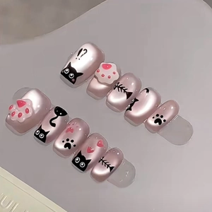 Detail of short pink press-on nails featuring black cartoon cat and fishbone patterns