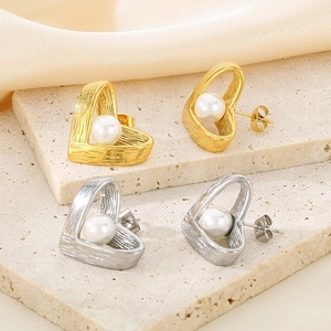 Detailed view of heart-shaped pearl stud earrings in gold and silver on silk