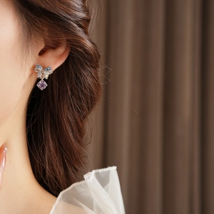 Close-up of bow earrings with blue rhinestones and purple gemstone pendant on model