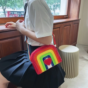 Rainbow crossbody bag with heart detail worn by model near a sunny window scene