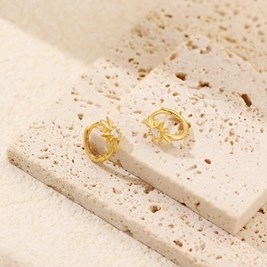 Macro detail of gold starburst earrings with clear zircon on a textured stone surface
