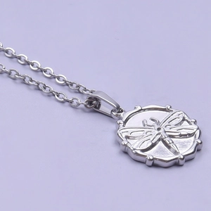 Macro shot of silver stainless steel pendant featuring a 3D embossed dragonfly on round charm
