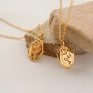 Detail of gold rose embossed oval pendant on a minimalist stainless steel chain