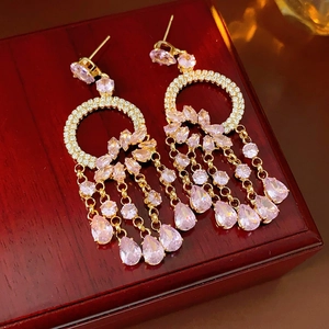 Detailed macro view of gold tassel earrings with pink zircon and teardrop stones