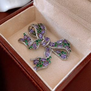 Macro detail of a bow-shaped brooch with purple and green crystals in a leather box