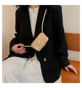 Détail d'un sac à bandoulière doré métallisé avec ornement papillon blanc sur blazer noir