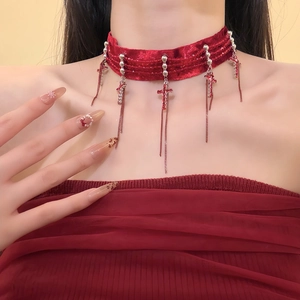 Detail of red velvet choker with silver cross pendant and tassel chain on model neckline