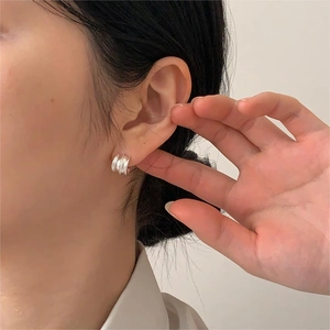 Close-up of three-layered silver curved hoop earrings worn on a model's ear