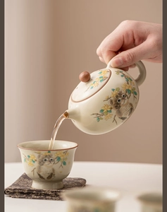 Action shot of Ru Kiln ceramic teapot pouring tea with hand-painted cat and floral patterns