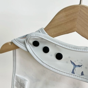 Close-up of waterproof baby bib with blue whale print and adjustable shoulder snaps