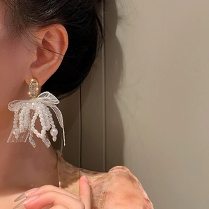 Close-up of golden bow earrings with white lace, pearls and tassels worn by a model