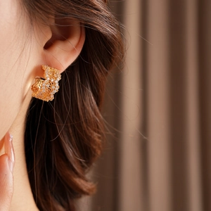 Close-up of golden hollow flower earrings with cubic zirconia on model's ear