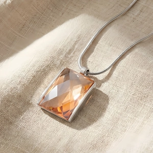 Detail of amber glass rectangular pendant on snake chain over beige linen fabric