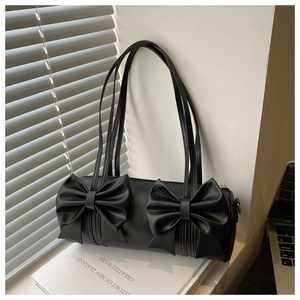 Detail of a black cylinder underarm bag with elegant bow accents on a book background