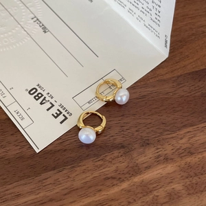 Elegant gold plated hoop earrings with round white pearls on a warm wooden background