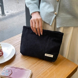 Detail of a black corduroy makeup bag held by a model over a wooden table setting