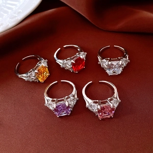 Macro shot of silver adjustable rings with colorful square zircons on deep red silk fabric