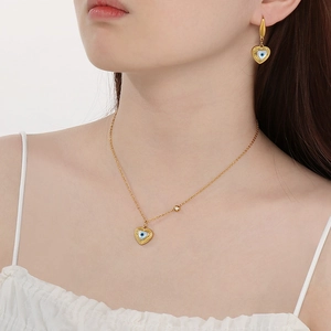 Detailed view of model wearing a gold heart-shaped evil eye necklace and earring set