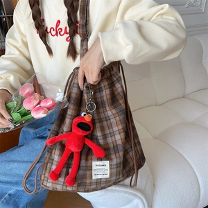 Detail of grey plaid drawstring backpack with knit texture and red plush pendant accessory