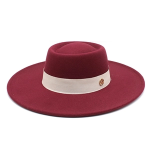 Close-up of a burgundy wool fedora hat with a beige fabric band and golden logo detail