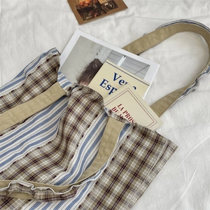 Detail of canvas tote bag featuring brown plaid and blue stripes on a white sheet