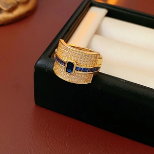 Detailed close-up of wide gold-plated ring with emerald cut blue stone and pavé zircons
