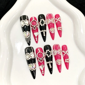 Unghie finte stiletto lunghe nere e rosa con cristalli di lusso e ciondoli in metallo