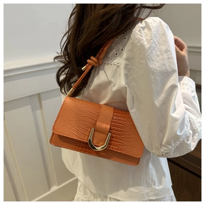 Detail of orange crocodile pattern bag with gold U-shaped hardware and knot strap