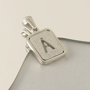 Macro shot of a silver rectangular pendant with a sandblasted finish and letter A cutout