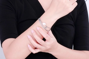 Silver double-layer chain bracelet with pearl and clover charms worn on a model's wrist