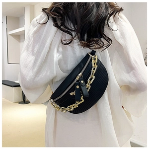 Detail of black woven chest bag featuring a chunky gold chain strap and sleek zip closure