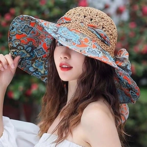 Close-up of straw sun hat featuring vibrant orange and blue paisley print ribbon and bow