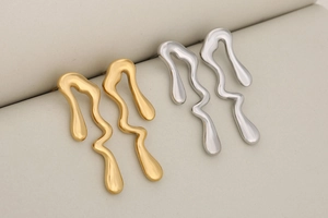 Détail de boucles d'oreilles en métal liquide doré et argenté aux formes fluides