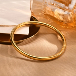 Polished gold stainless steel bangle displayed on elegant warm golden silk fabric