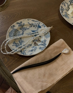 Flat lay of baroque pearl necklace, silver heart studs and hairpin on vintage floral plate