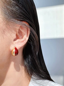 Close-up of model wearing teardrop earrings in polished gold and deep red enamel finish