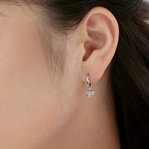 Detail shot of a silver heart drop earring with a clear gemstone on a female ear