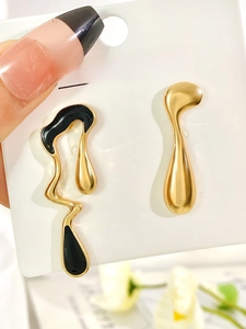 Macro detail of asymmetric liquid teardrop earrings in black and gold metallic finish