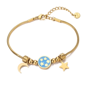 Detail view of gold star and moon charms with blue enamel on a stainless steel bracelet