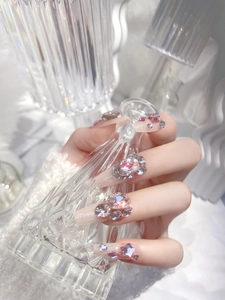 Detail view of pink press-on nails featuring large sparkling rhinestones and star accents