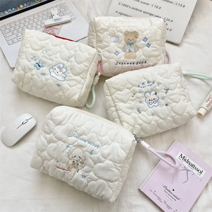 Macro detail of white quilted heart patterns and cute cartoon animal embroidery on makeup bags