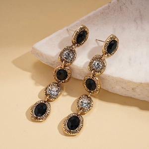 Elegant gold earrings with black and clear rhinestones on white marble background