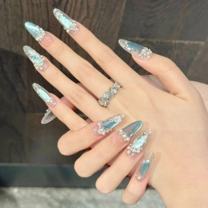 Dettaglio di unghie a mandorla lunghe con sfumatura blu, perle e strass 3D scintillanti