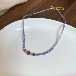 Close-up of faceted purple amethyst beads necklace with golden spacers on a white plate
