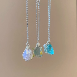 Macro detail of wire-wrapped natural stone pendants in purple, green, and blue on silver chains